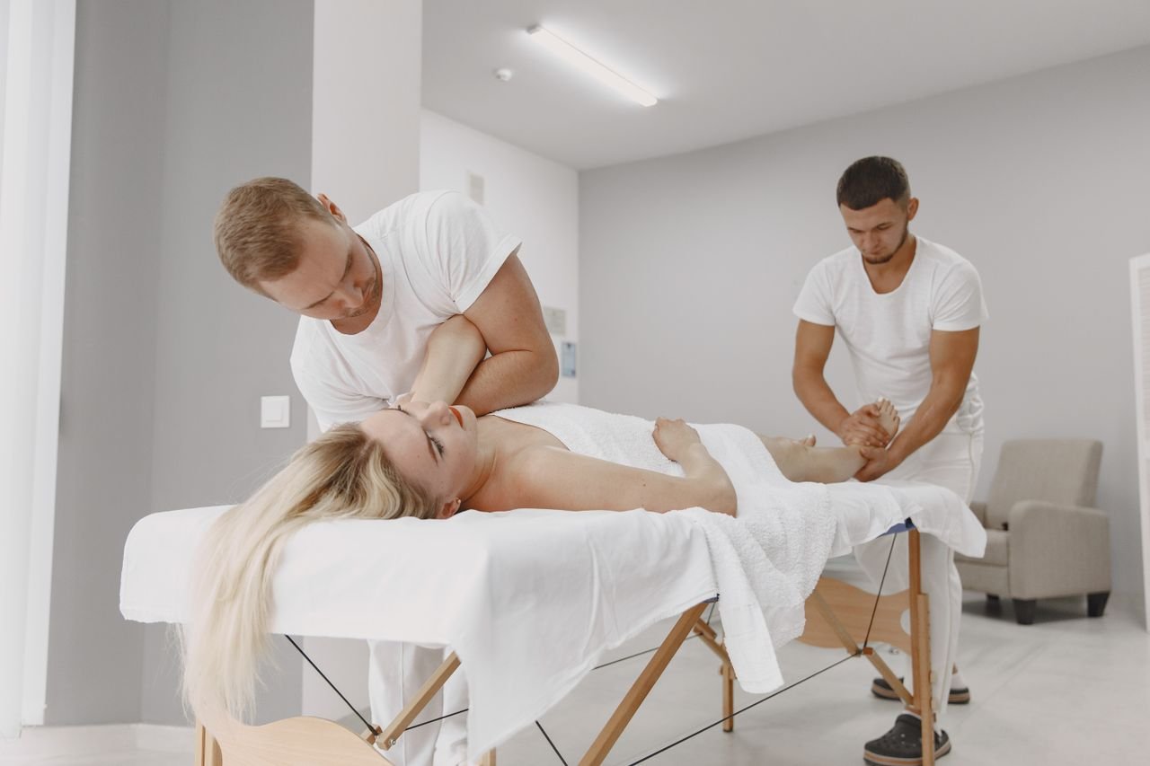 A woman receives a professional massage from two masseurs in a modern spa setting, promoting relaxation and wellness.