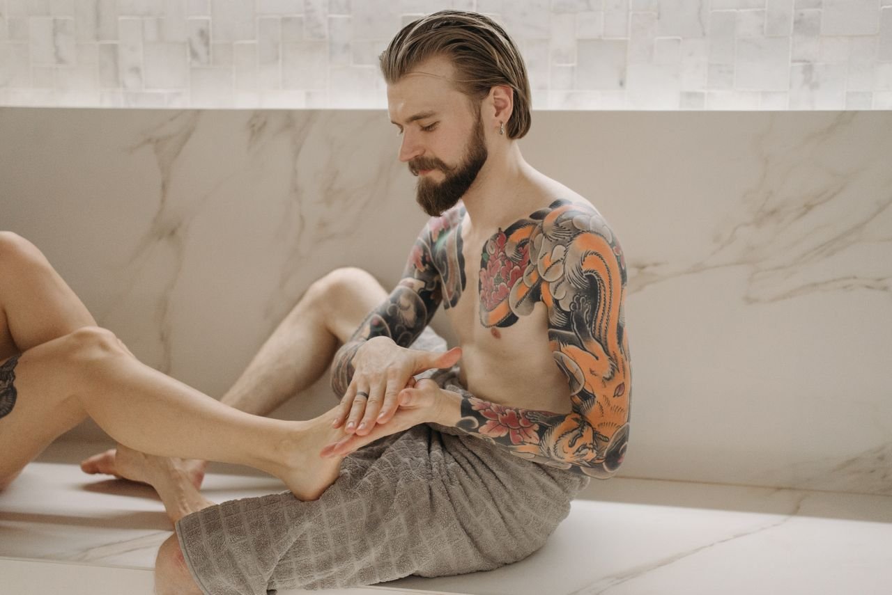 A tattooed man receives a foot massage indoors, showcasing vibrant body art.